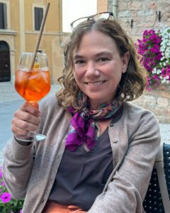 Yvette enjoying an Aperol Spritz in the picturesque town of Spello, Italy, surrounded by charming architecture and vibrant flowers.